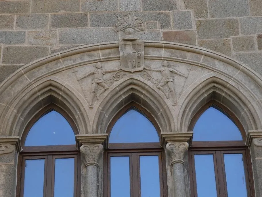 Ventana trífora neogótica coronada por un escudo